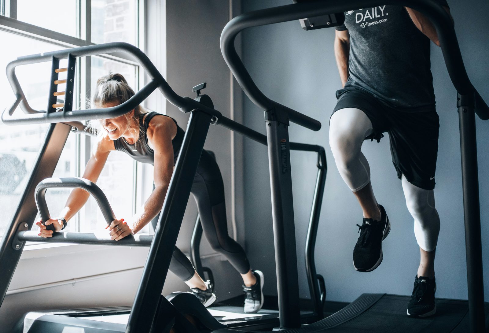 Two people running on incline treadmills, representing HIIT and steady-state cardio training