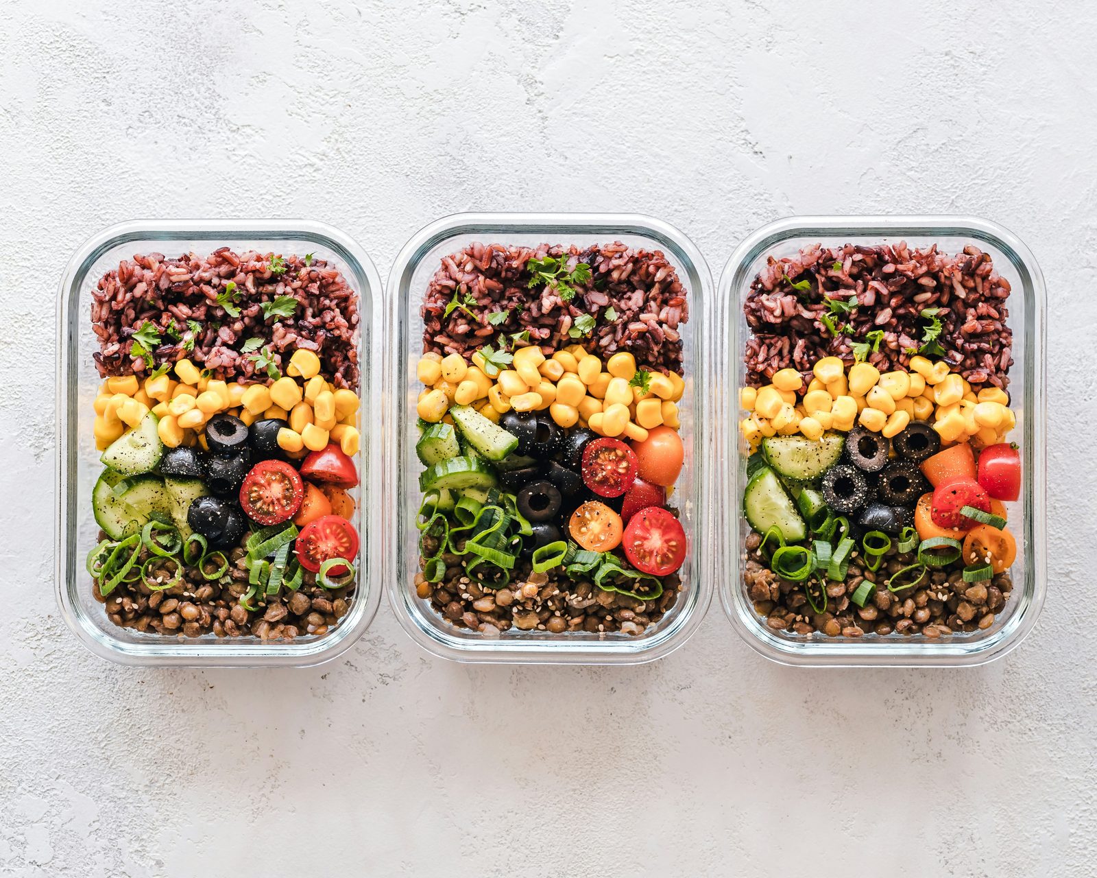 Three meal prep containers with rice, lentils, and vegetables, representing meal prep versus eating out