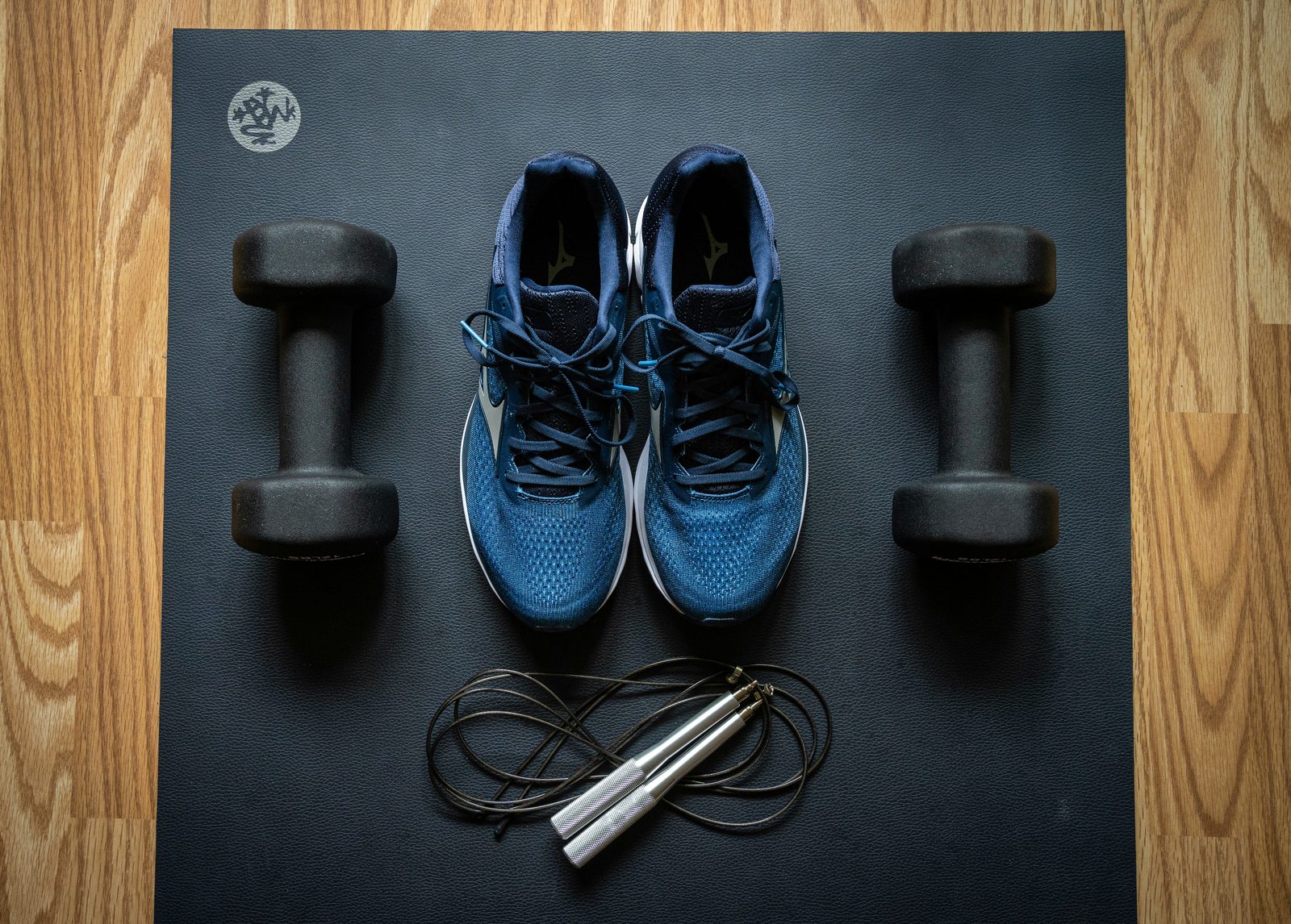Running shoes, dumbbells, and a jump rope on a gym mat